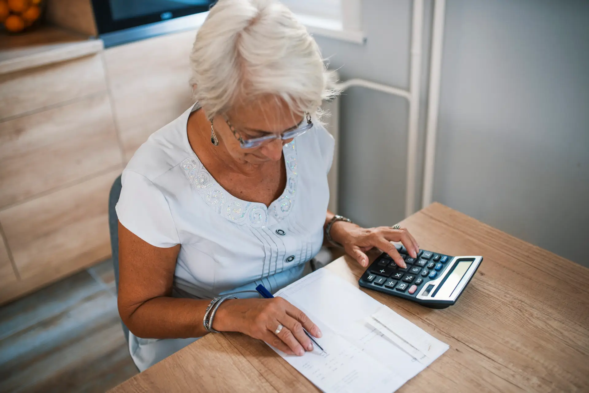 business, savings, annuity insurance, age and people concept - senior woman with papers or bills and calculator writing at home. Senior woman calculating taxes at home